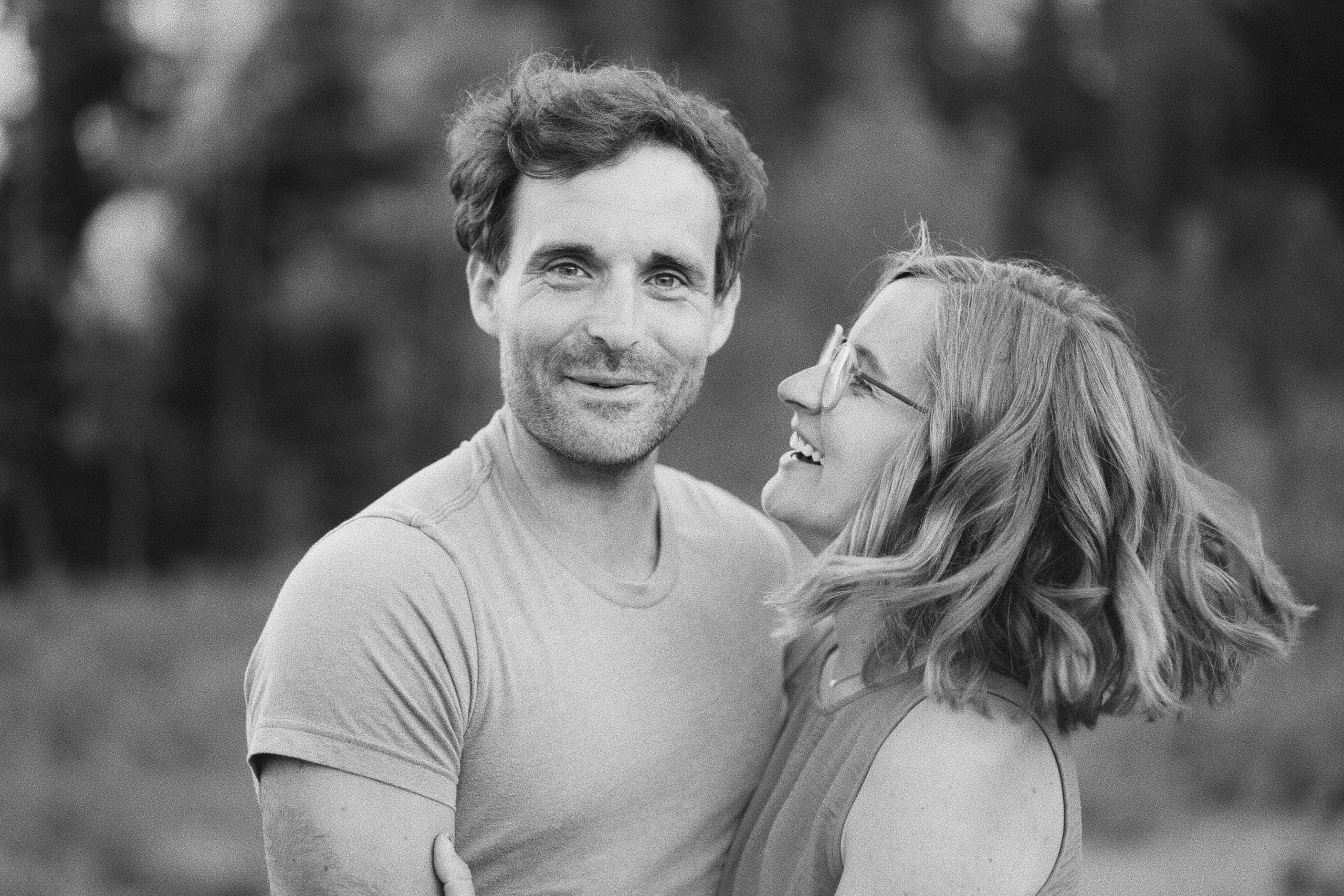 Black-and-white close-up of a couple, the man smiling at the camera as the woman laughs looking up at him.