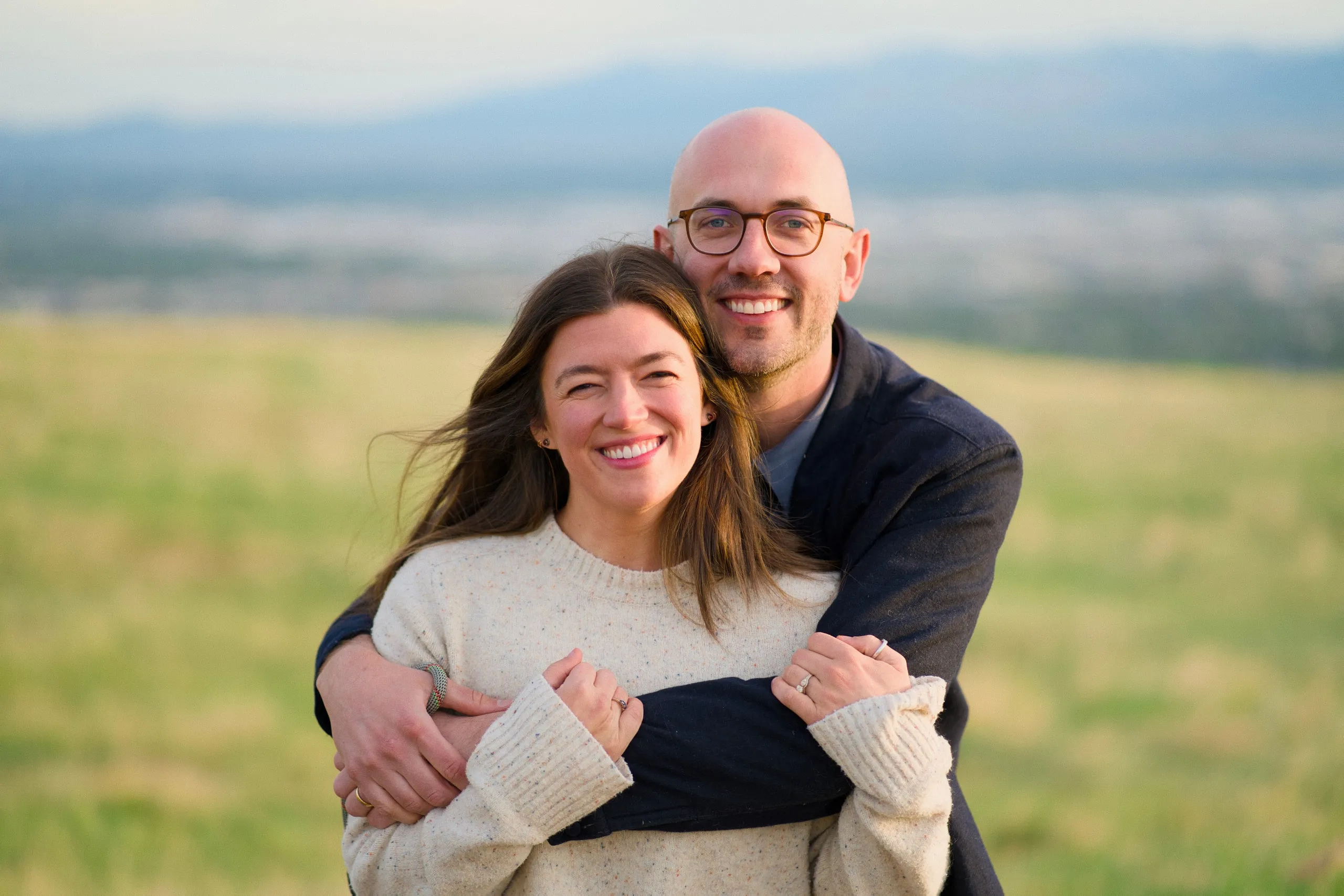 Close-up of a couple embracing and smiling, with a soft green field behind them.