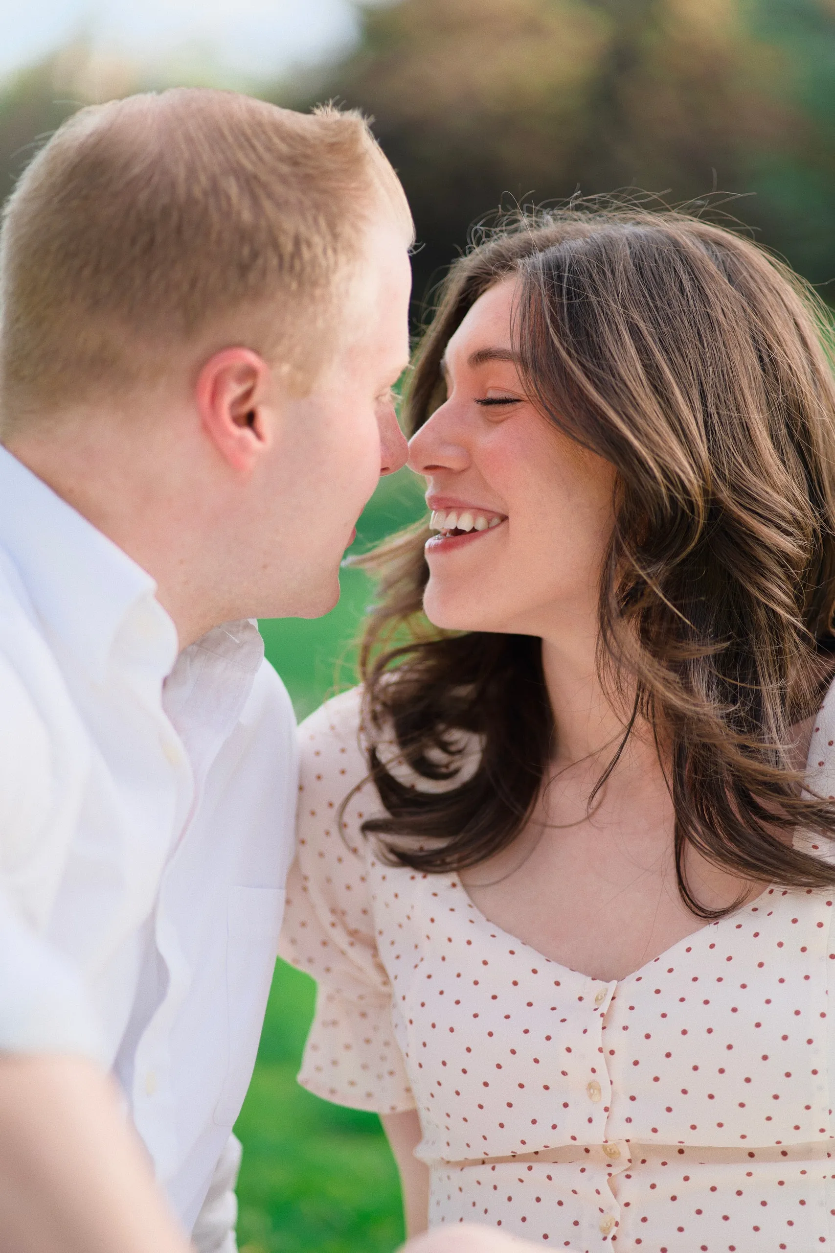 Close-up of a couple about to kiss, the woman laughing in soft sunlight.
