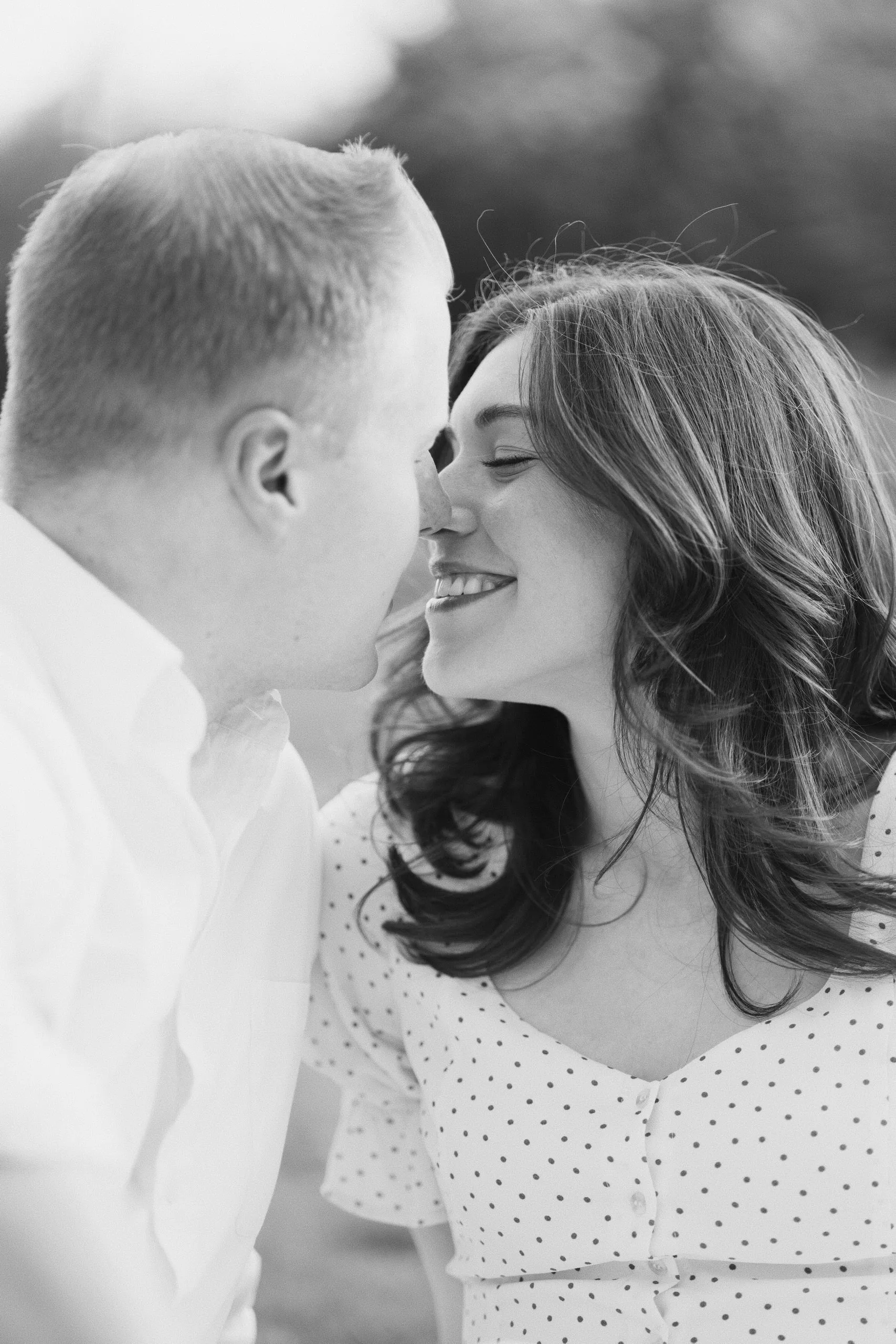 Black-and-white close-up of a couple nose to nose, the woman smiling brightly.
