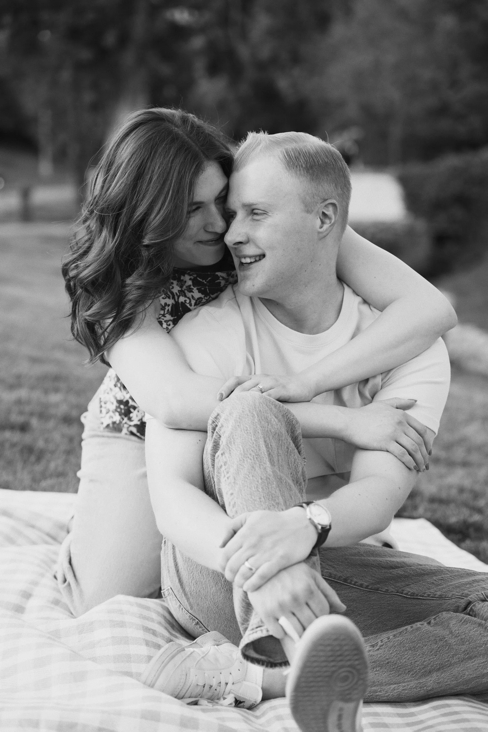 Black-and-white photo of a couple snuggled together on a picnic blanket, smiling.