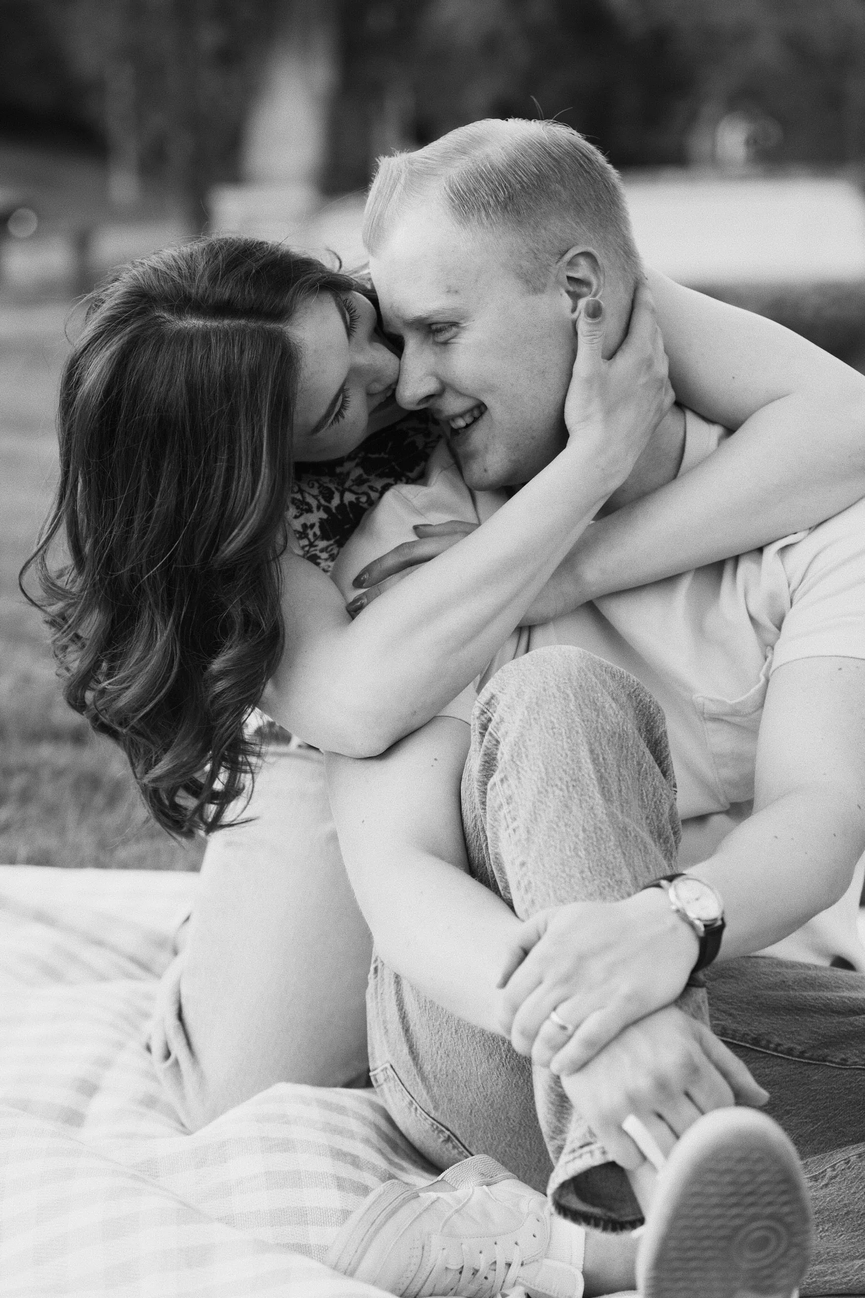 Black-and-white photo of a couple on a blanket as the woman kisses the smiling man's cheek.
