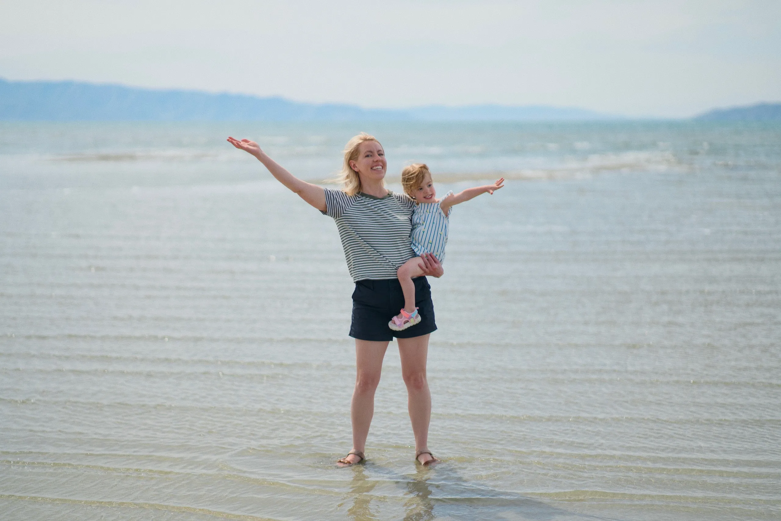 A woman holds her young daughter in the shallows of the Great Salt Lake, both stretching their arms out wide.