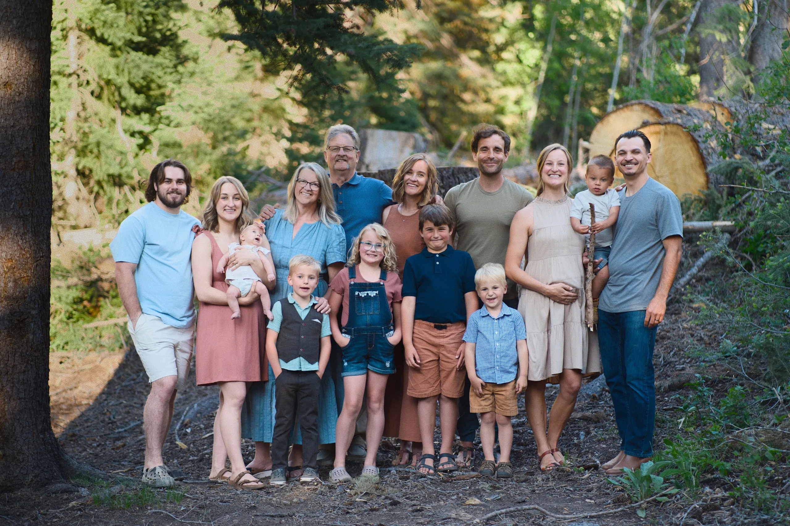 A large extended family of adults and children, including a baby, gather for a group portrait in the forest.