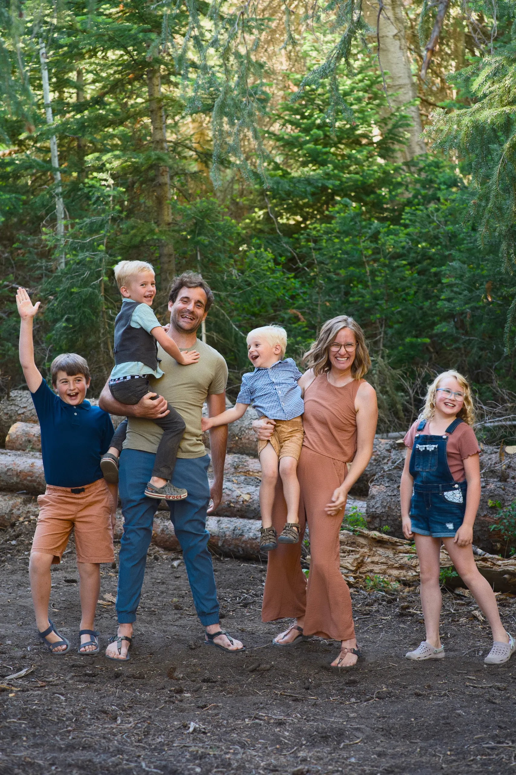 A family of six being playful in the woods — a toddler on dad’s shoulders, the older children waving and laughing.