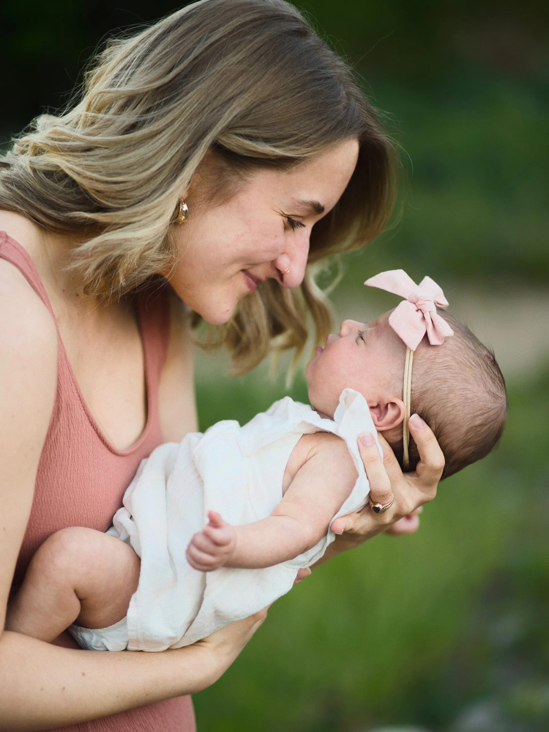 A mother holds her newborn daughter nose to nose, the baby wearing a pink bow headband.